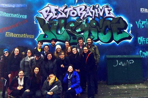 Spring break in Northern Ireland group photo in front of "Restorative Justice" graffiti