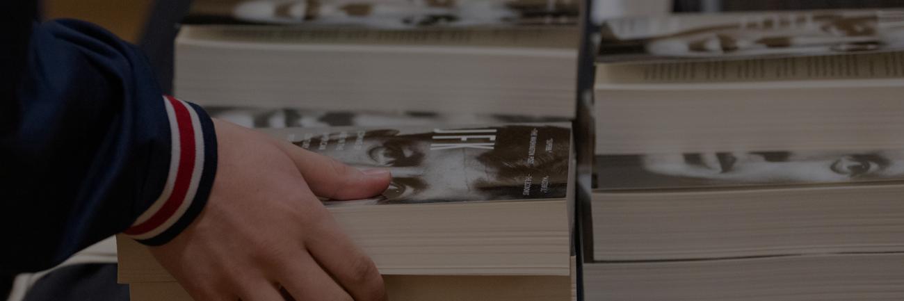 Student picking up a stack of JFK books