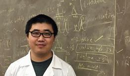 Yue Tang in white lab coat, in front of blackboard