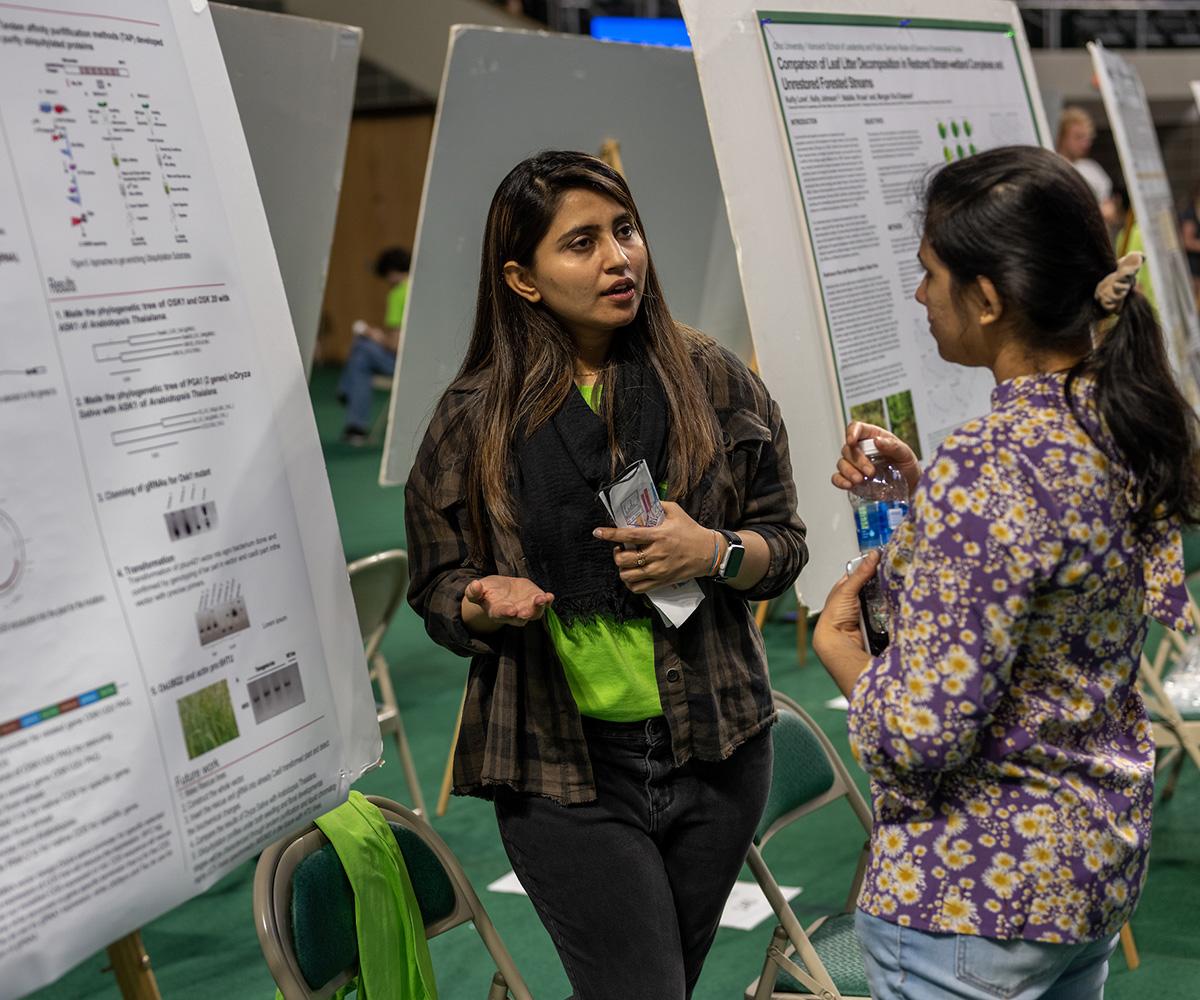 Two students talk about the research presented on a poster board.