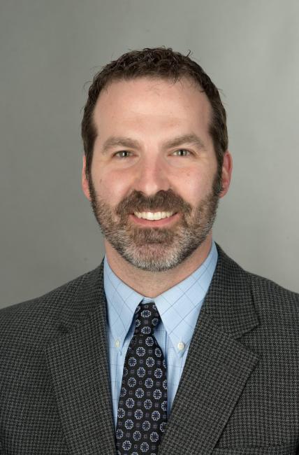 Headshot of a smiling Michael Kopish with a moustache and beard wearing a dark suit and tie.