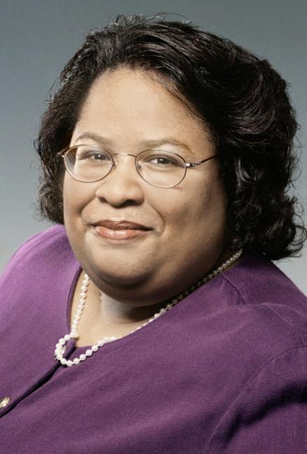 Headshot of a smiling Tasha Attaway wearing glasses and a purple jacket with pearls.