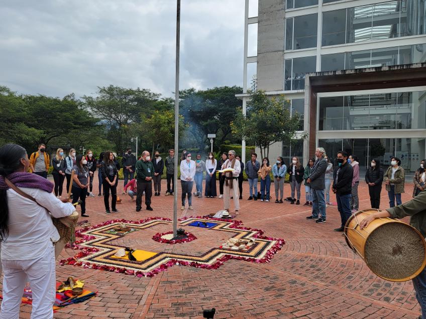 A group of people gathers around fruits, grains and vegetables nicely placed on the ground. This is a welcome ceremony in Ecuador for students.