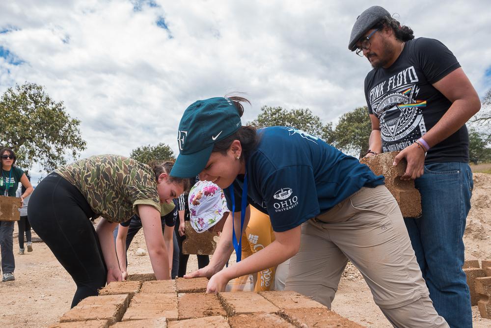 A group of volunteers moves blocks to build a house in Bellamaria Community