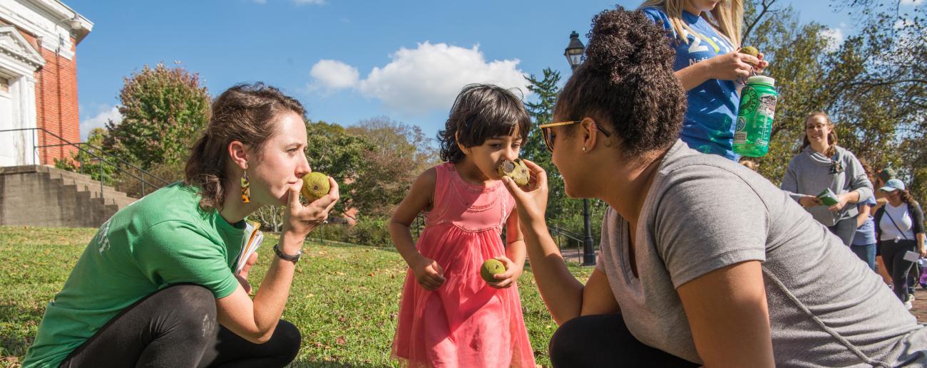 Two students interacting with child outdoors