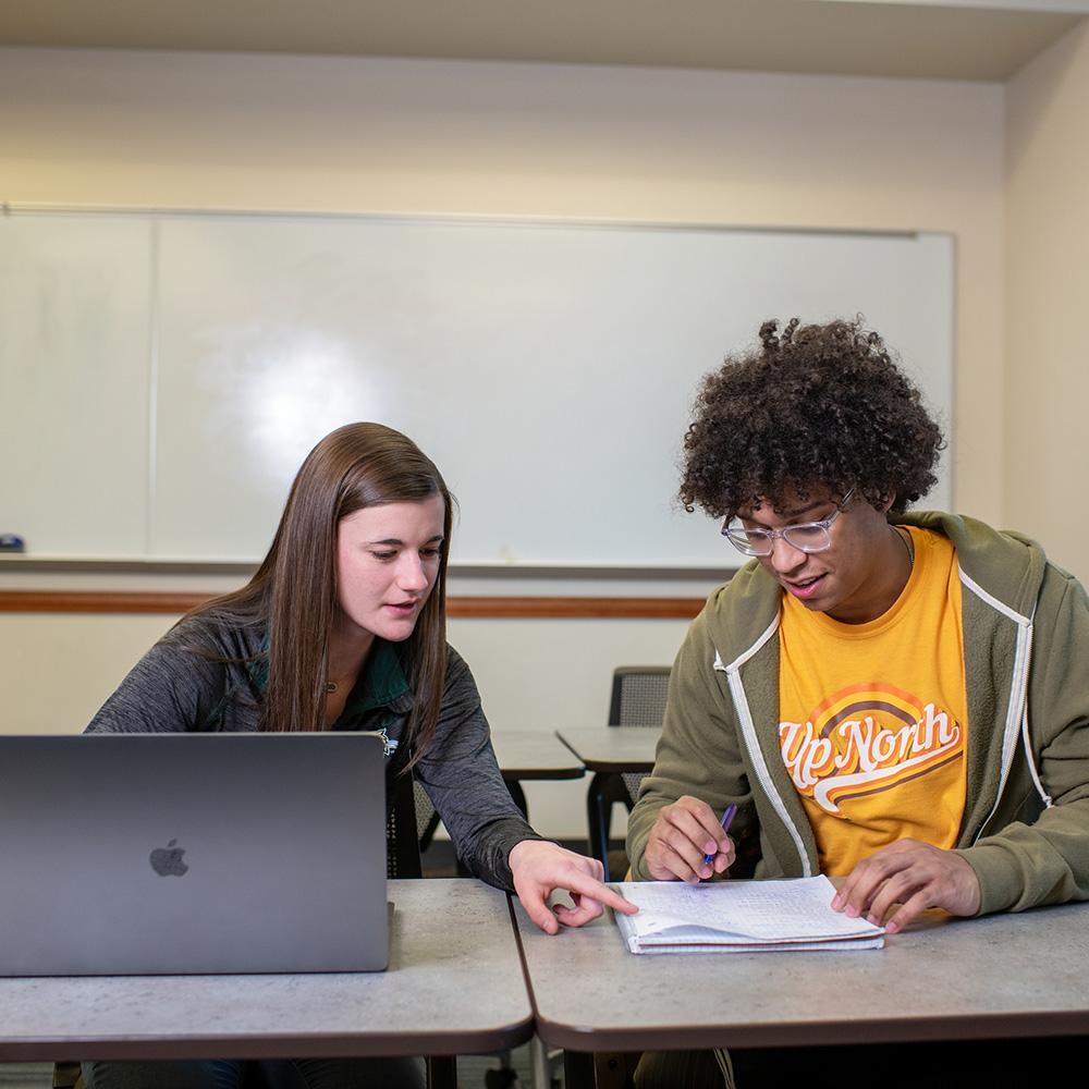 Two students study together with a laptop and pencil and paper