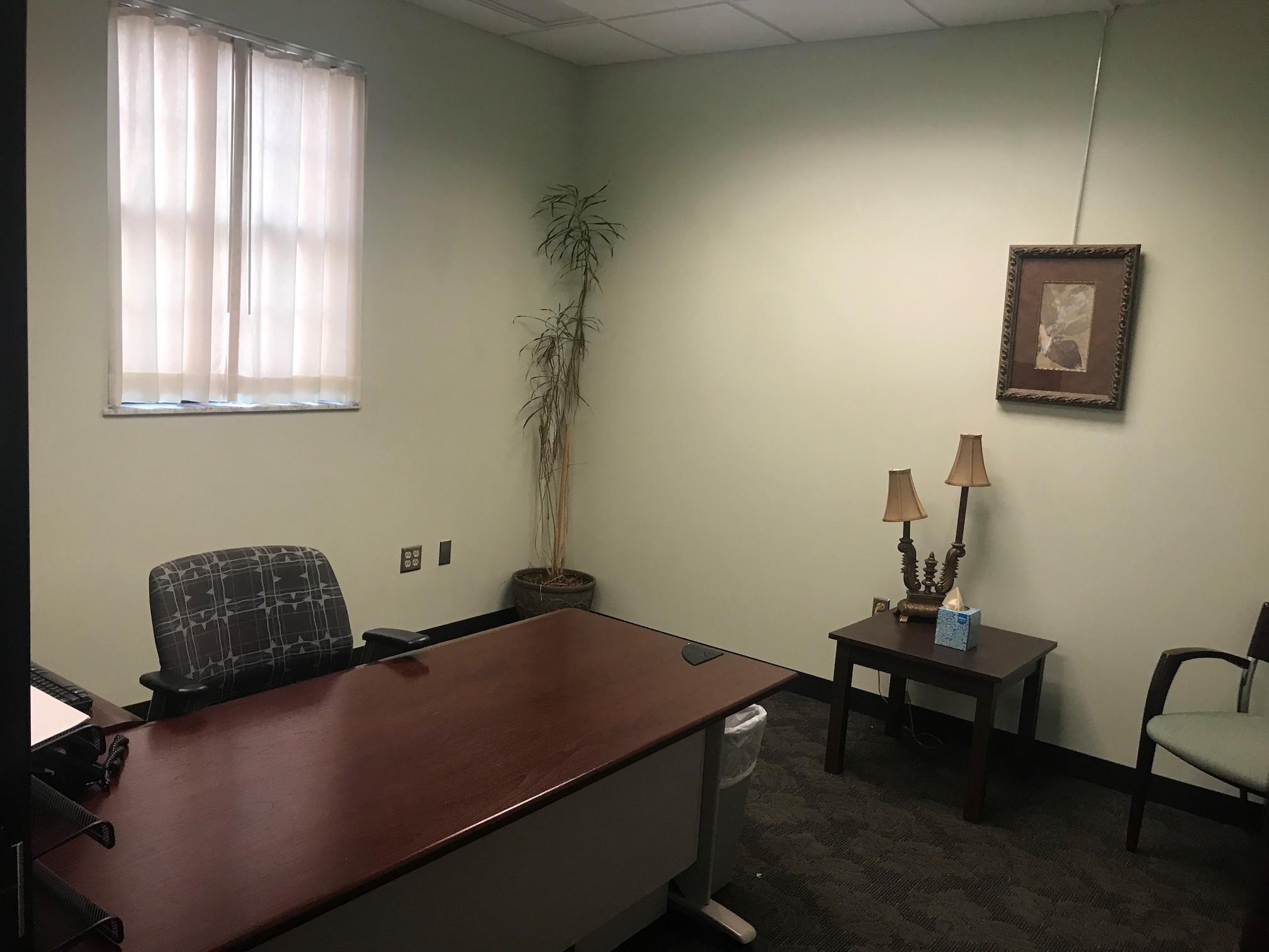 Office for one person, with a desk, office chair, and other furniture, and a curtained window behind the desk