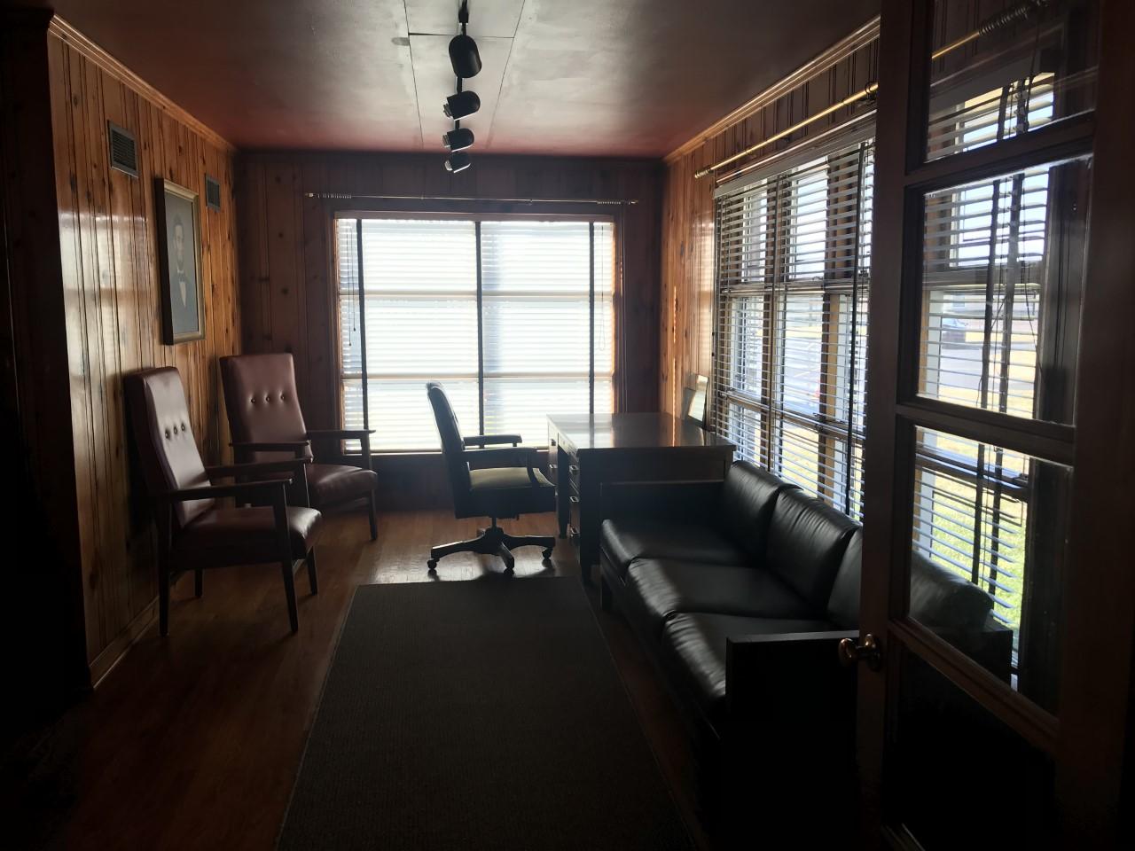 Living room with wood paneled walls and wood floors, wide and tall windows covering most of two walls