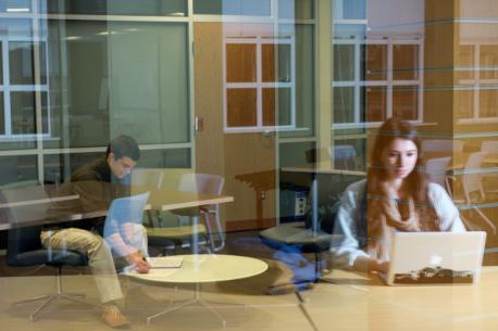 A student viewed through a glass window using a laptop computer