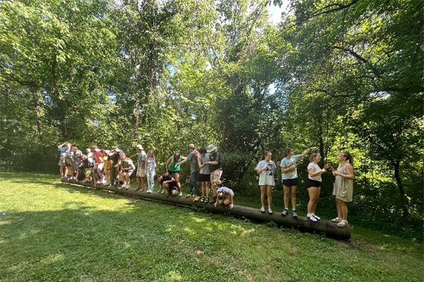 Students balance on a log in the forest