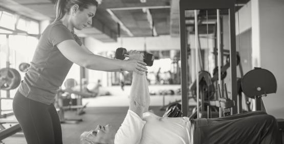 Trainer assisting client with weights in fitness center