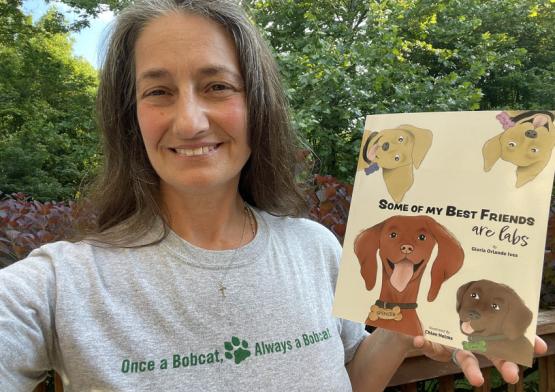 Gloria (Orlando) Ives, BSC ’88, shows off her Bobcat pride and her first book, which was designed by OHIO student-now-graduate CJ Herr, BFA ’22.