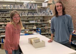 Two students pose for a picture with library shelves in the background