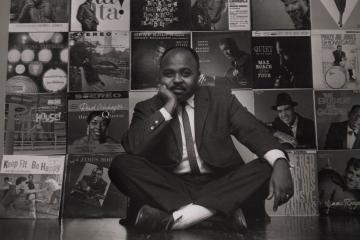 Chuck Stewart sitting in front of a wall of album covers he had taken