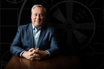 Perry Sook '80 poses for a portrait behind a desk wearing a suit