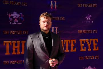 A man poses for a photo in front of a movie poster backdrop