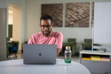 A young man sitting at a table with a laptop.