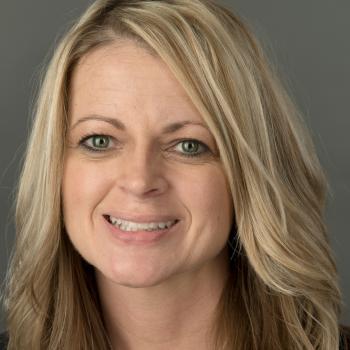 Amy Meeks Headshot. Woman with long blonde hair smiles at the camera infant of a gray backdrop.