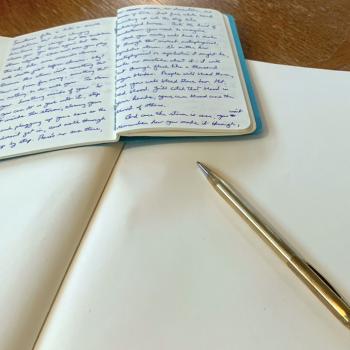 A notebook with writing lays on top of a blank notebook by a pen.