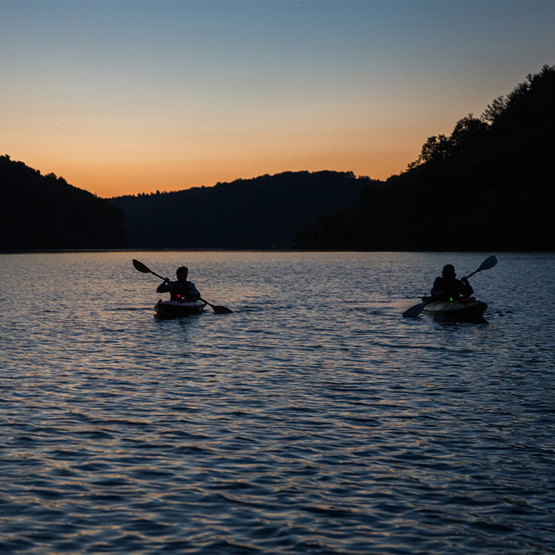 Two people paddle on water at night.