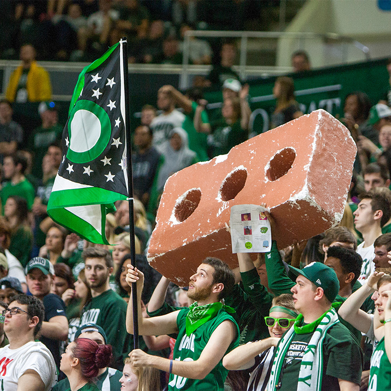 Students hold a giant brick and green flag at a basketball game.