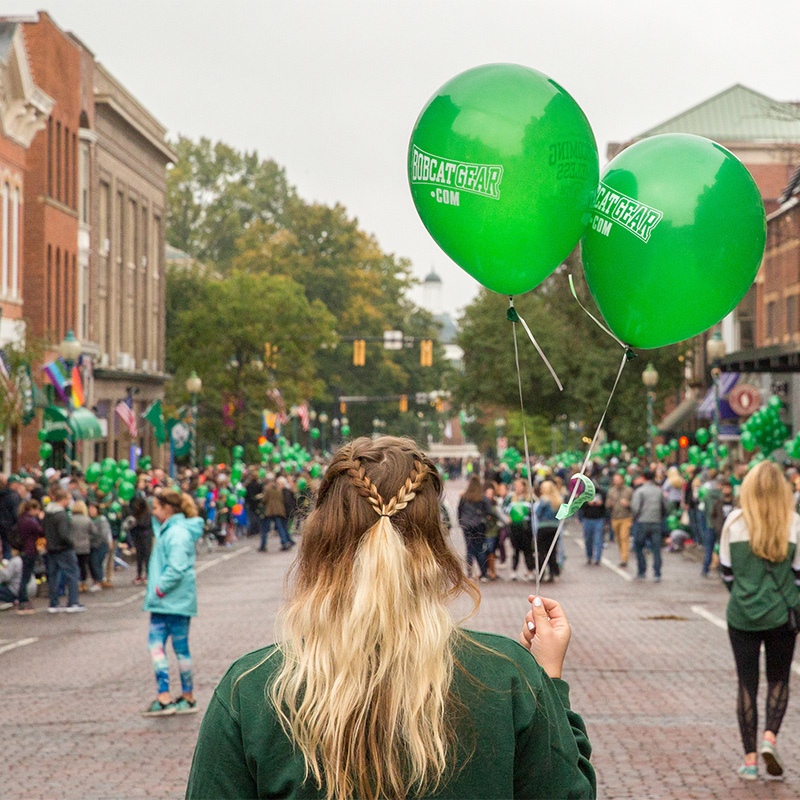 A person holds two green balloons at homecoming.