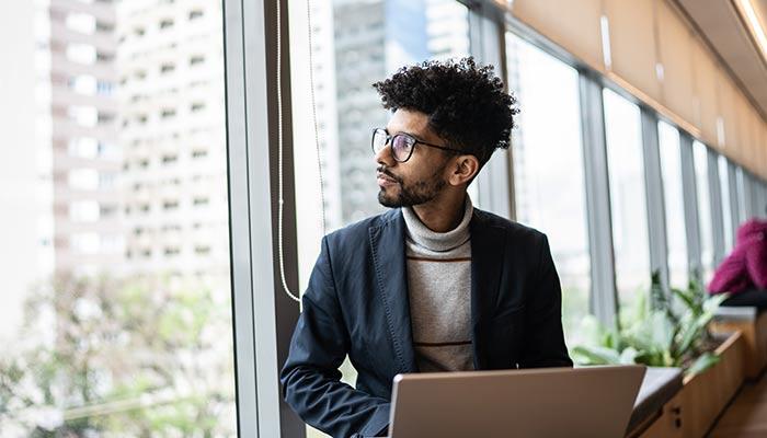 Man with laptop looking out of window.