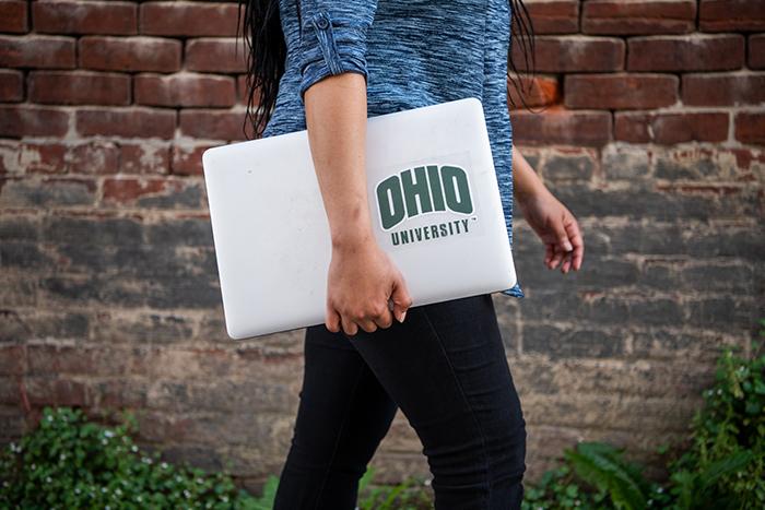 Student carrying laptop on campus with Ohio university sticker