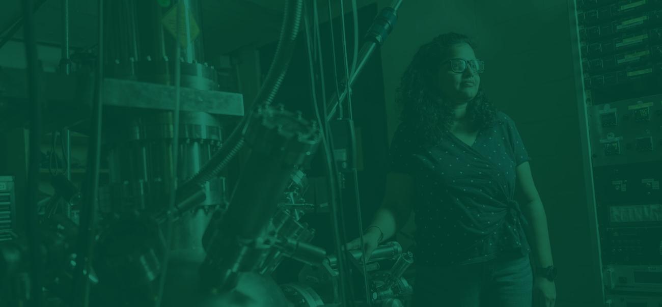 Physics student stands among scientific equipment