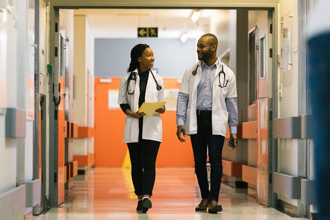 A man and woman in white jackets with stethoscopes walking down hallway