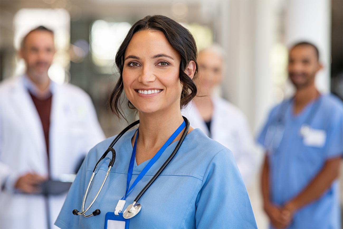 Smiling brunette woman in blue scrubs standing in front of other medical professionals