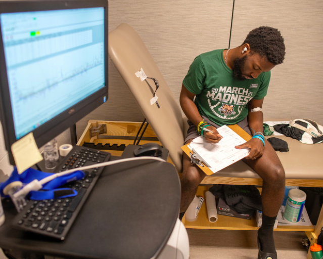 Exercise physiology student writes in a notebook while reviewing a screen monitor