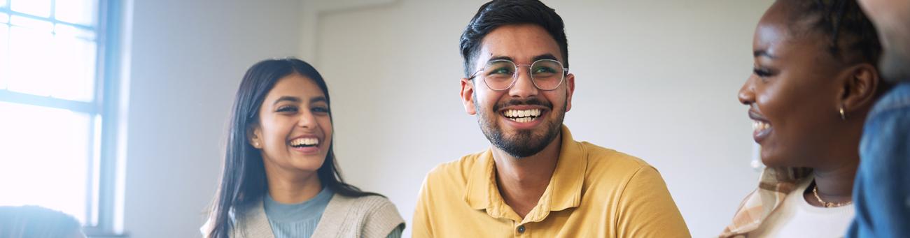 4 students sitting, smiling and talking in a classroom setting