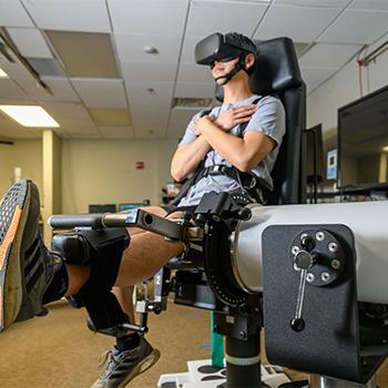 An individual does knee exercises on a machine while wearing 3D goggles.