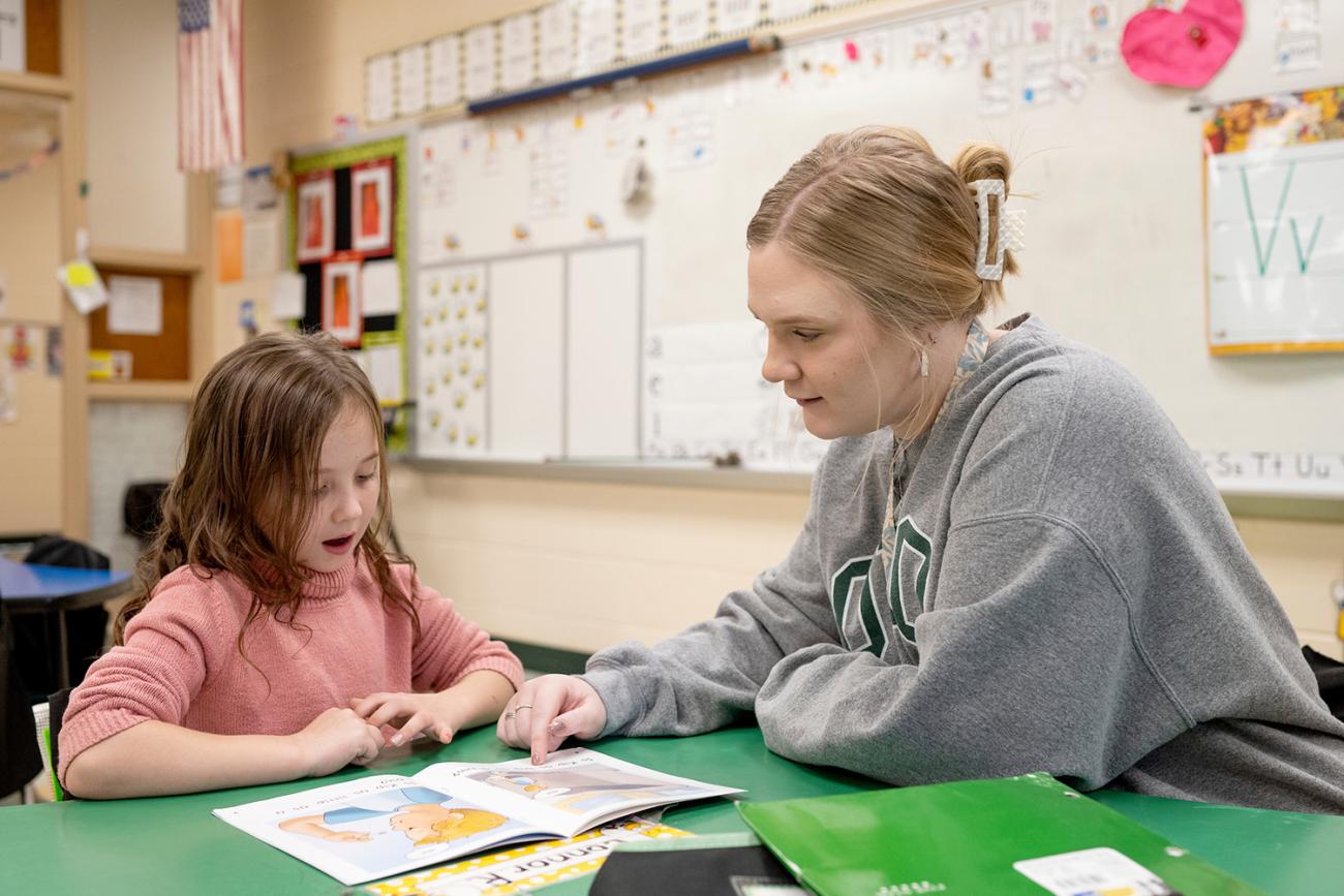 Teacher listening to young female student reading