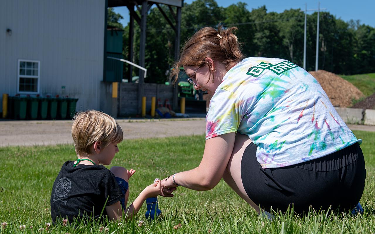 a child and adult talking while sitting in the grass. backs are toward the camera