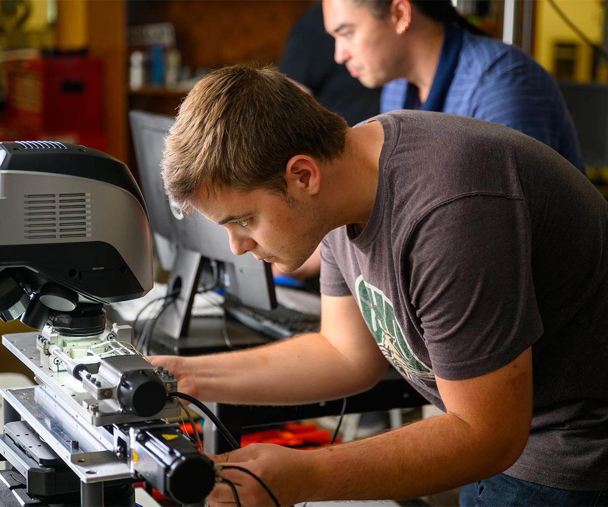 A student looks in a microscope while doing research in a lab.