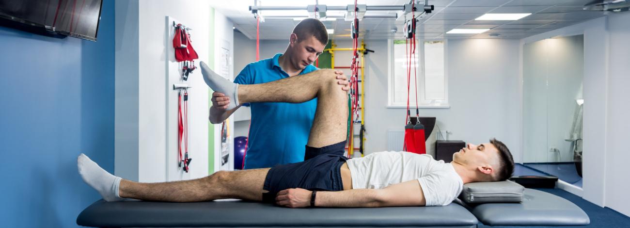 An athletic trainer stretching the leg of a patient.