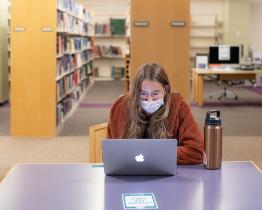 Student on laptop masked in Alden Library
