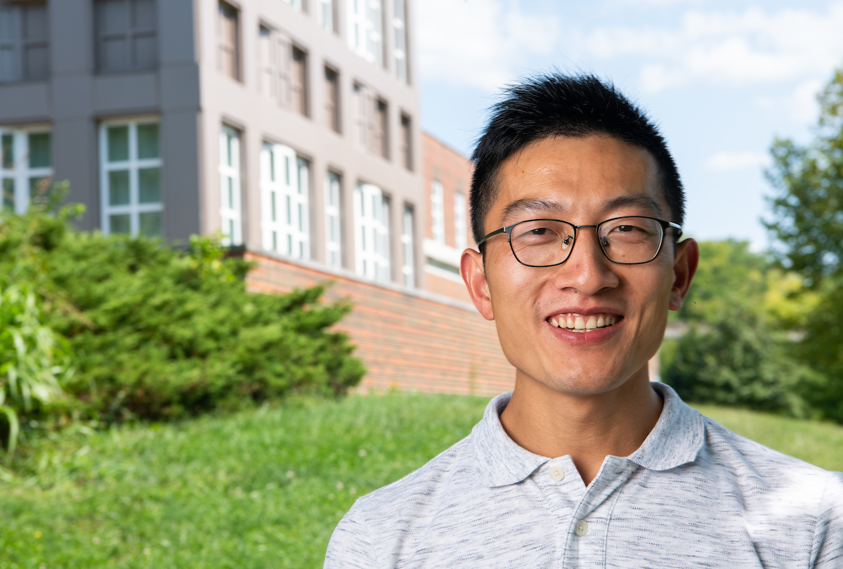 Dr. Shouan Zhu portrait with bushes, grass and brick building in background