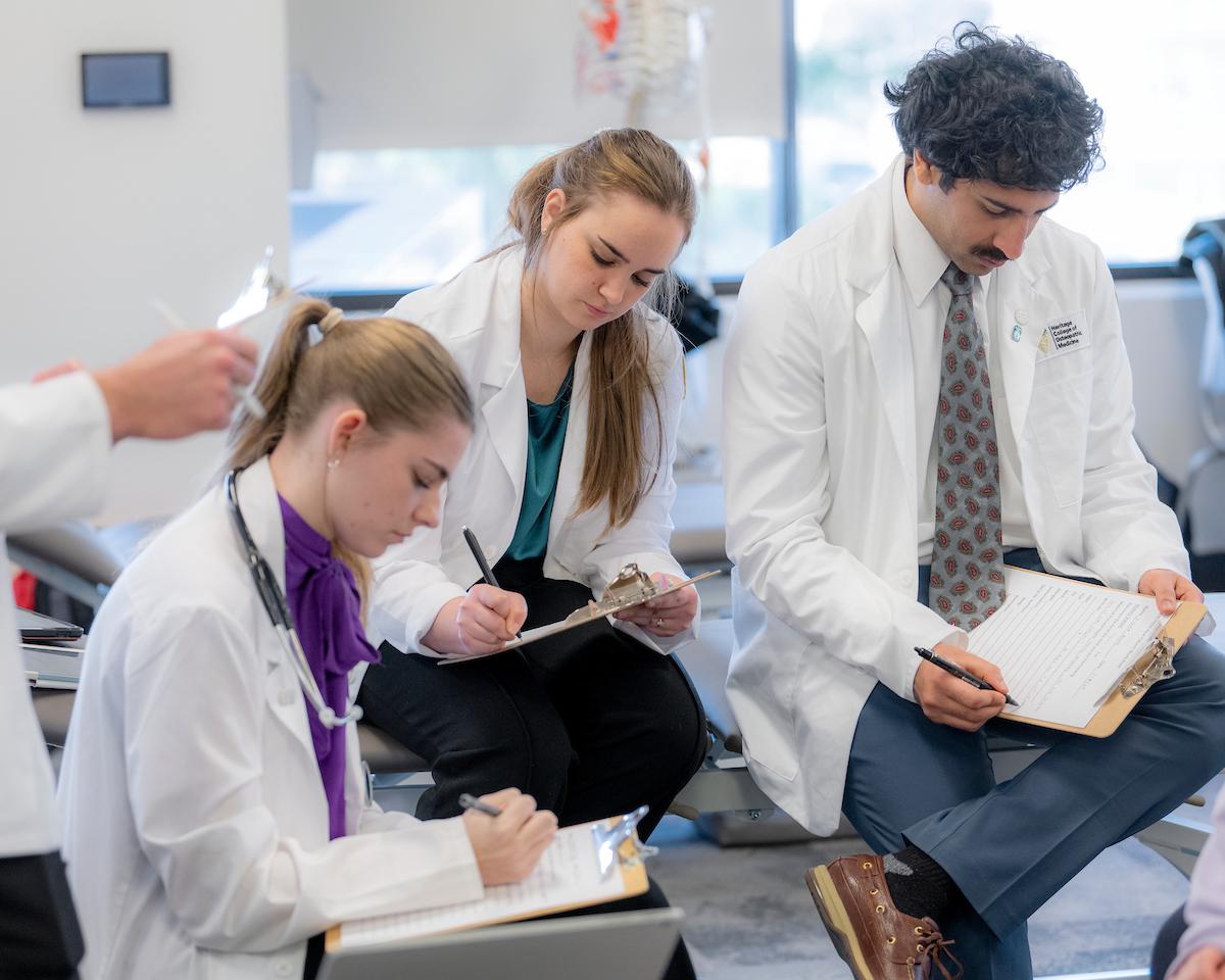 Medical students write on clipboards in their whitecoats