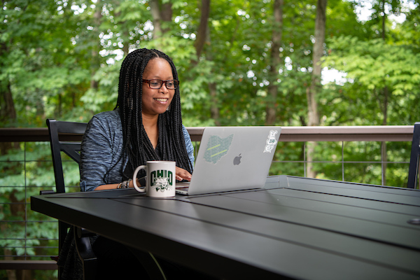 Ohio University student sits on her porch, typing on a laptop with an OHIO mug