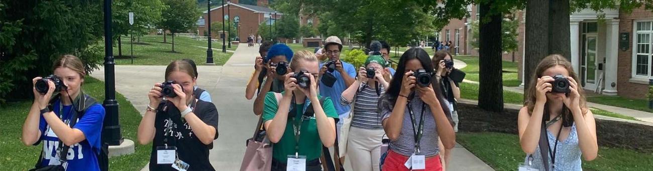High School Journalism Workshop participants walk in a group aiming cameras at the viewer