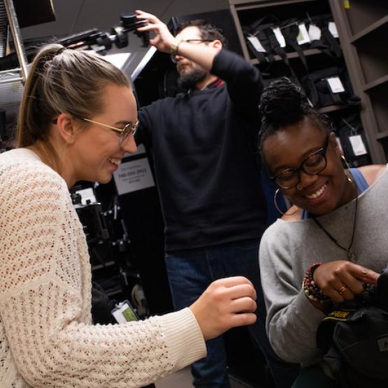 Two students look at a camera in the MDIA Equipment Room
