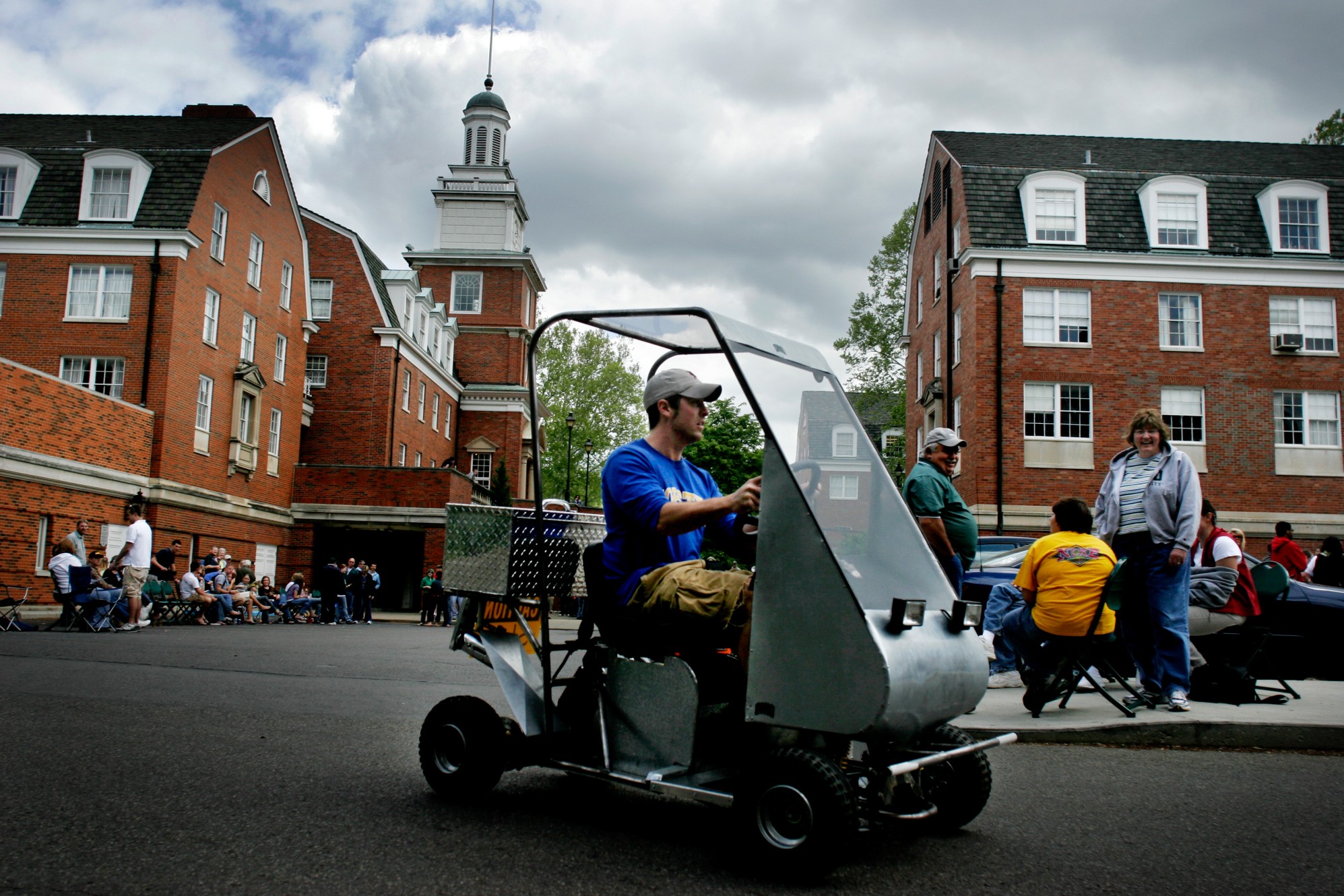 Male student in blue shirt and white baseball cap drives a mini car in front of Stocker Center