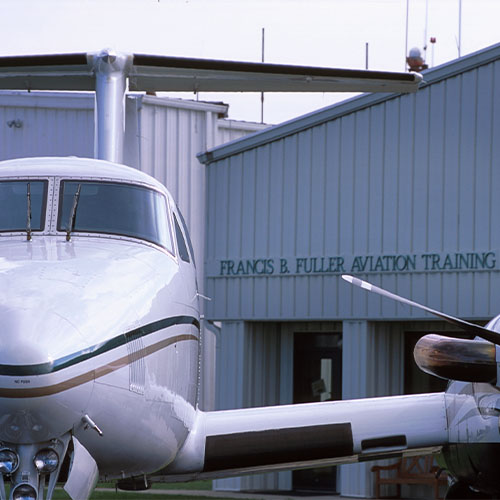 Small airplane in foreground, hanger with words "Francis B. Fuller Aviation Training" in background