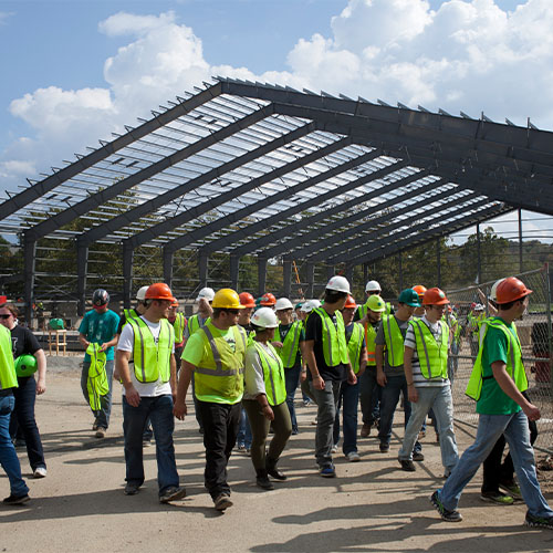 Students in hard hats and neon vests walk in front of beam structure