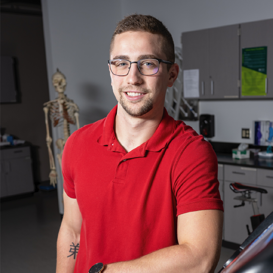 A exercise physiology student poses in front of a skeleton model in the classroom