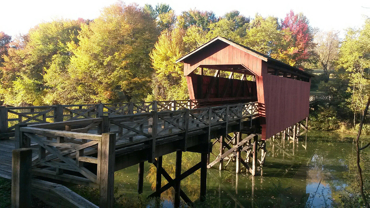 A covered red bridge that sits high over a pond.