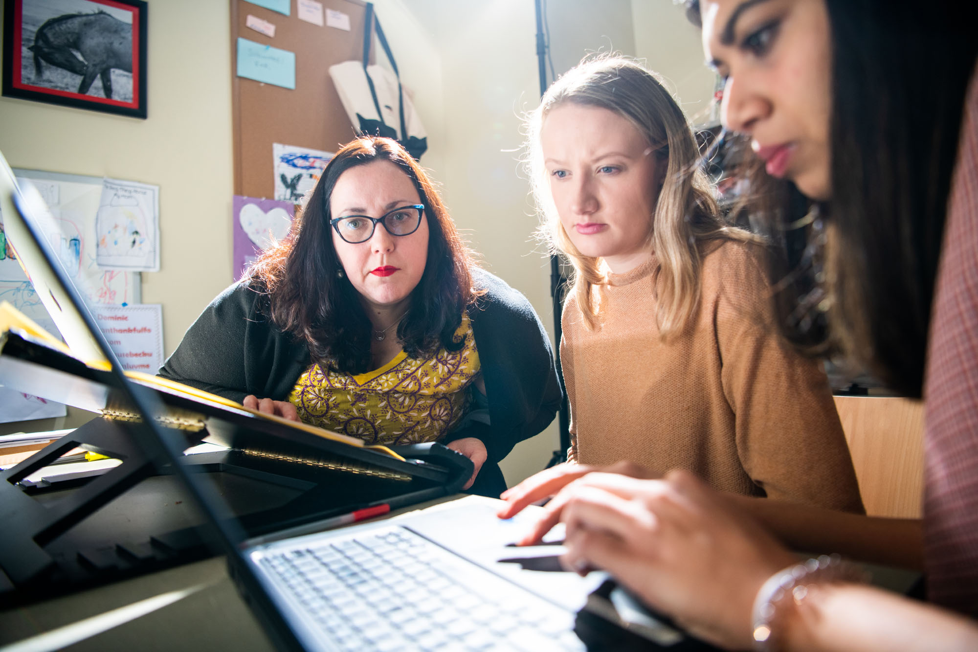 A professor watches intently as students complete work on a laptop computer